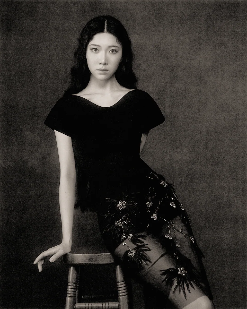 Sammi Chen seated in a black dress against a charcoal backdrop.
